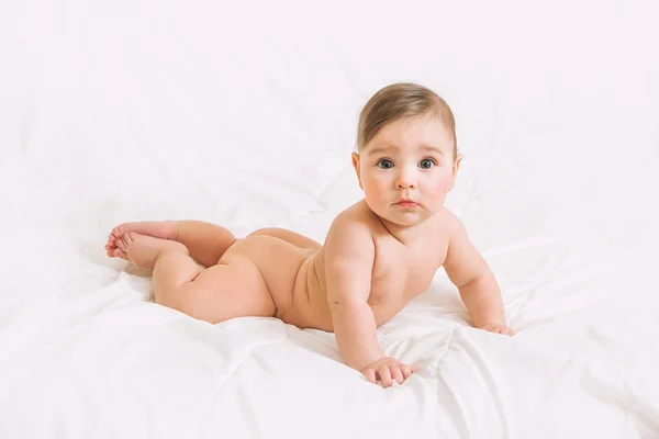 Naakte verrast babymeisje liggend op witte bed — Stockfoto