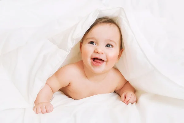 Gelukkig Baby ligt op bed onder de deken — Stockfoto