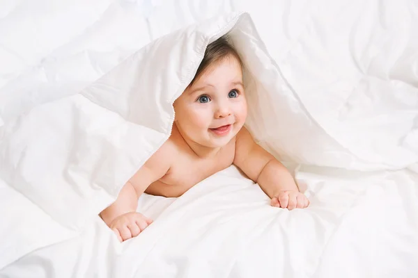 Surpreendido Bebê jaz na cama sob o cobertor — Fotografia de Stock