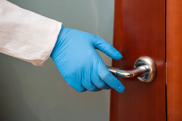 Hand in einen blauen Medizinhandschuh, der die Türklinke hält — Stockfoto