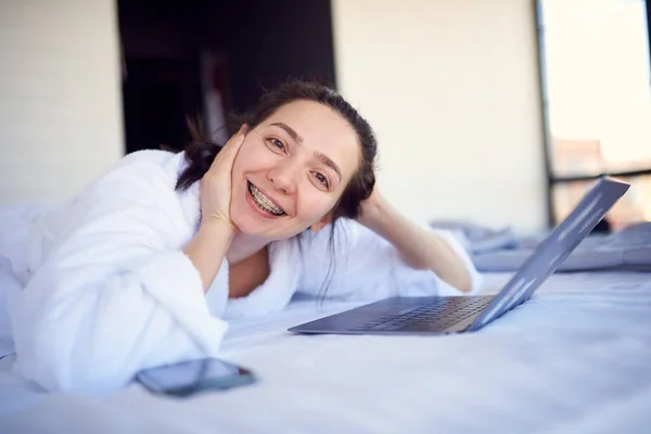 Chica Con Aparatos Ortopédicos Albornoz Una Cama Con Ordenador Portátil —  Fotos de Stock