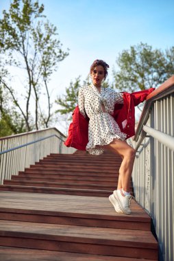 Kırmızı ceketli ve beyaz elbiseli güzel kız merdivenlerde dans ediyor.