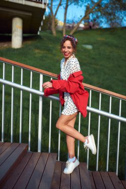 Cheerful girl climbs the stairs in a short white dress with a red jacket in the spring park