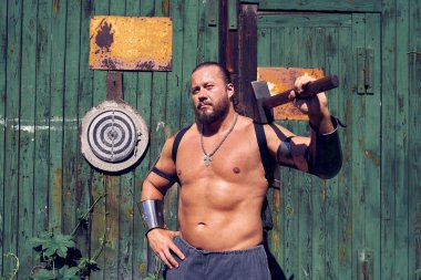 Big muscular man with a hammer against the background of green wooden wall
