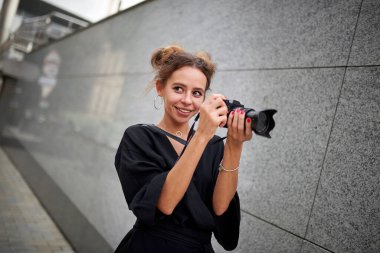 Pretty girl photographer in a black dress with a camera on the background of a marble wall