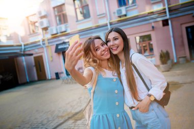 İki genç ve sevimli kız arkadaş dışarıda telefonda selfie çekiyorlar..