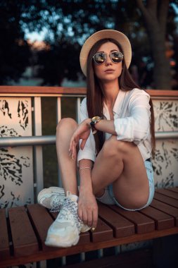 Güneş batarken bir yaz parkında hasır şapkalı ve güneş gözlüklü tatlı ve genç bir esmer.