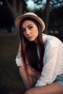 Gün batımında bir yaz parkında hasır şapkalı tatlı ve genç esmer.