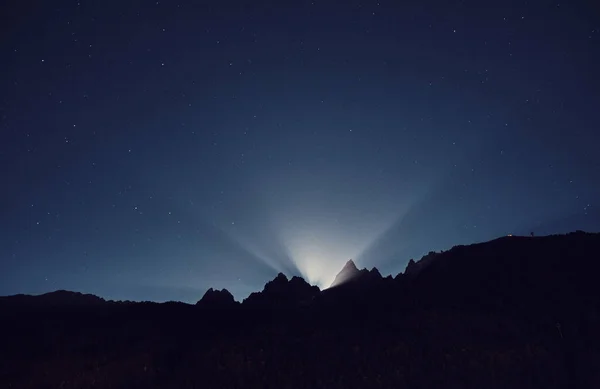 The light of the rising moon from behind the mountains. Night mountain landscape. Alps, France.