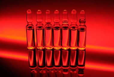 Virüse karşı kırmızı neon arka planda cam ampullerde aşı.