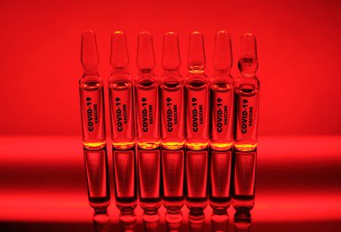 Kavram. Coronavirus / COVID-19 ampullerde kırmızı neon arkaplan üzerinde aşılar.