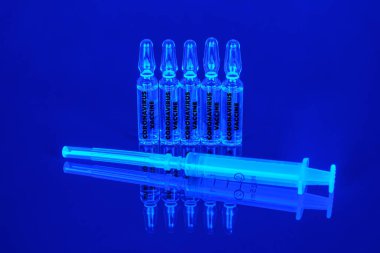 Kavram. Coronavirus / COVID-19 ampullerdeki mavi neon arka plan aşıları.