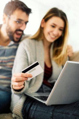 Mutlu çift oturma odalarında kredi kartları ve laptoplarıyla online alışveriş yapıyor.