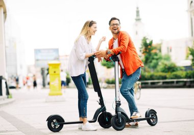 Genç çift şehirde elektrikli scooter sürerken eğleniyor.