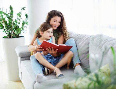 Anne ve iki oğlu evdeki kanepede kitap okuyorlar.