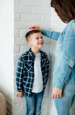 Mother measuring the height of her son on the wall at home