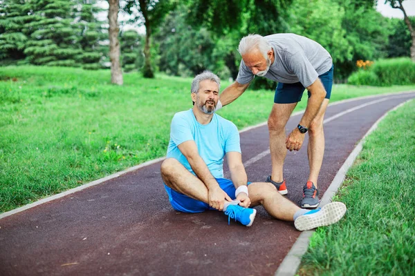 Outdoor senior fitness man lifestyle active sport exercise injury pain ache leg knee ancle help support friend — Stock Photo, Image