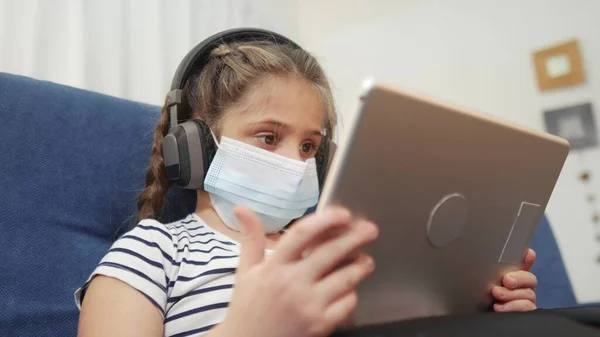 distance learning online a lessons. child girl with digital tablet in mask studying remotely at home. school education coronavirus online lessons lockdown concept. child learns distance learning