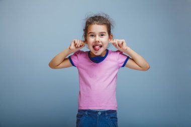 dil kulak çeker gösterilen kız çocuk üzerinde gri bir arka plan dalga geçiyor.