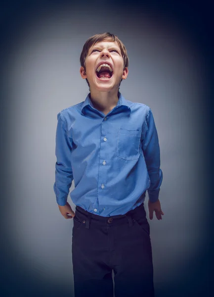 Chico adolescente grita mirando arriba en un gris fondo cruzado proceso — Foto de Stock
