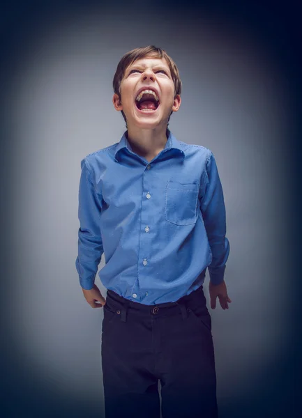 Boy teenager yells looking up on a gray background cross process — Stock Photo, Image