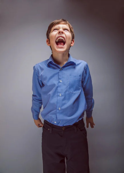 Niño adolescente grita mirando hacia arriba en un fondo gris — Foto de Stock
