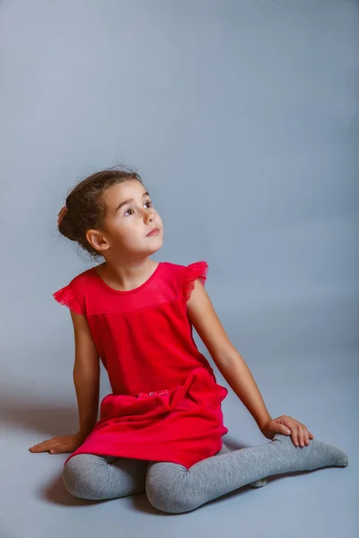 Calm girl teenager sits in a red dress looking to the side on — Stock Photo, Image