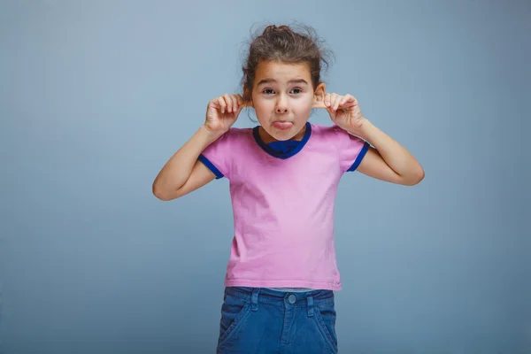 Child girl showing tongue pulls ears on gray background — Stock Photo, Image