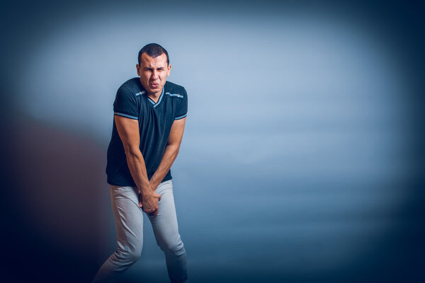 Европейский человек, держащий руки над пахом от боли на сером
