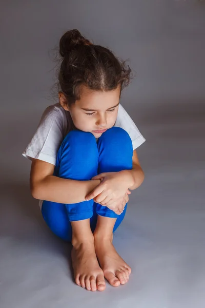 Дівчина спить, обіймаючи ноги на сірому фоні — стокове фото