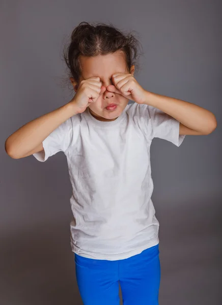 Menina bebê chora esfrega seus olhos em um fundo cinza — Fotografia de Stock