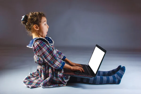 Menina criança em um vestido no fundo cinza procurando computador — Fotografia de Stock