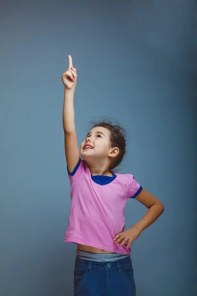 Ragazza bambino che punta verso il cielo su uno sfondo grigio — Foto Stock