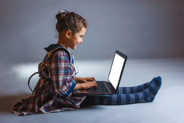 Mädchen Kind sitzt beim Spielen Laptop auf einem grauen Hintergrund — Stockfoto