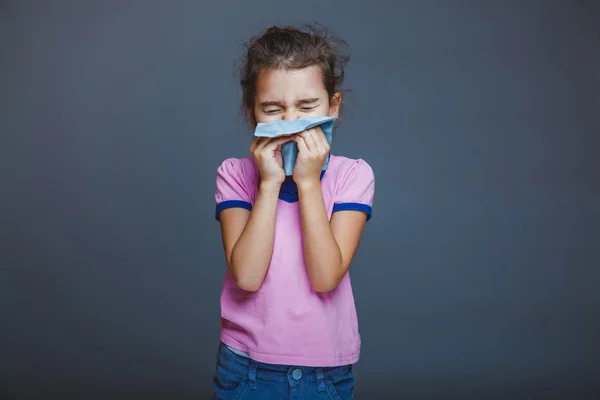 Menina criança espirra em lenço em um fundo cinza — Fotografia de Stock