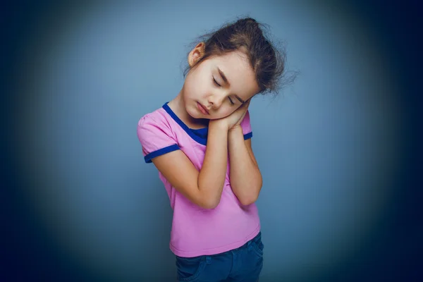 Girl child wants to sleep hands under her cheek on a gray backgr — Stock Photo, Image