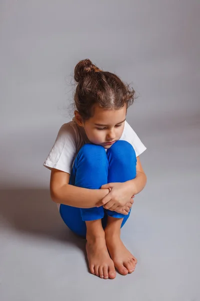 Ragazza abbracciato le gambe addormentato su uno sfondo grigio — Foto Stock