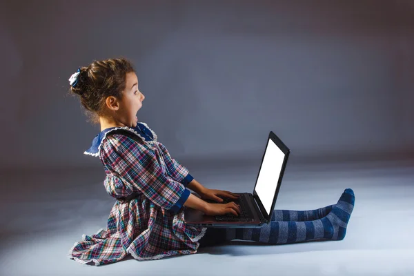 Mädchen suchen Computer auf einem grauen Hintergrund Überraschung — Stockfoto
