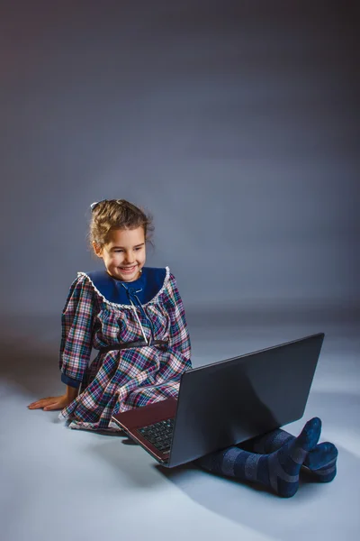 Little girl looking at laptop rejoices over gray background art — Stock Photo, Image