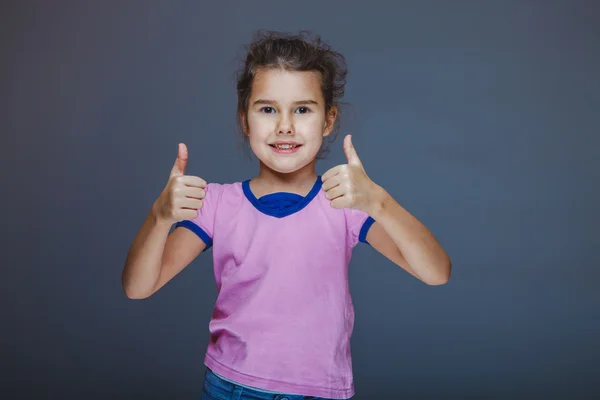 Liten flicka visar tecken ja fingrar på grå bakgrund — Stockfoto