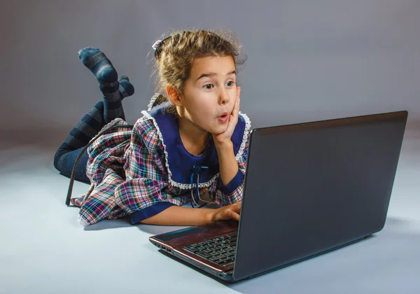 Menina adolescente jogando no chão em um notebook cinza backgroun — Fotografia de Stock