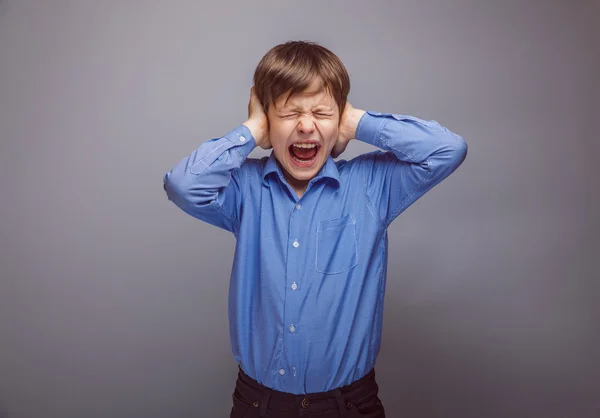 Tiener jongen die betrekking hebben op zijn oren schreeuwen handen op een grijze backgro — Stockfoto