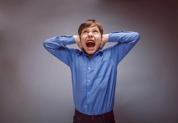 Teenager boy shouts shut ears opened his mouth on a gray bac — Stock Photo, Image