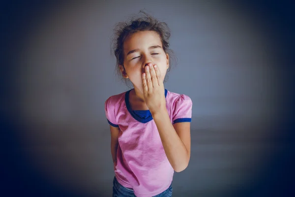 La niña está cansada cierra la boca bosteza en un backgro gris — Foto de Stock