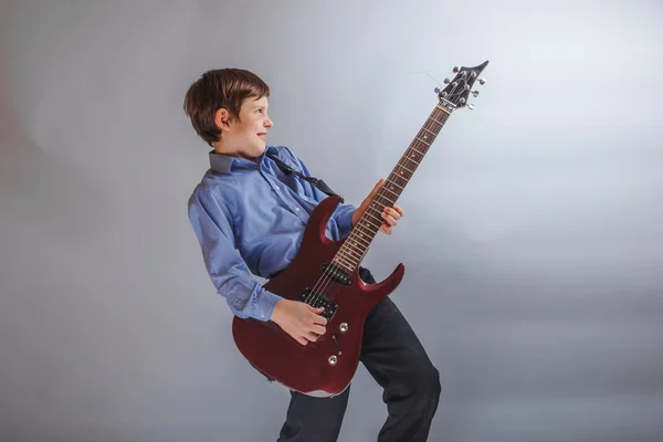 Ragazzo adolescente aspetto europeo suonare la chitarra su un retro grigio — Foto Stock