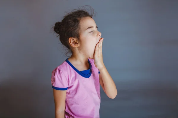 Bambina chiude la bocca sbadiglia su sfondo grigio — Foto Stock