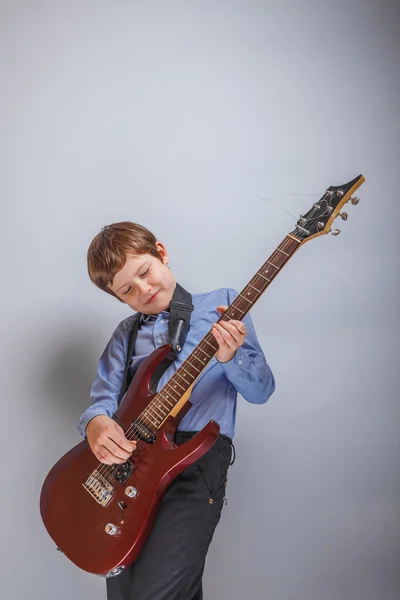 十代の少年が灰色の背景でギターを弾く — ストック写真
