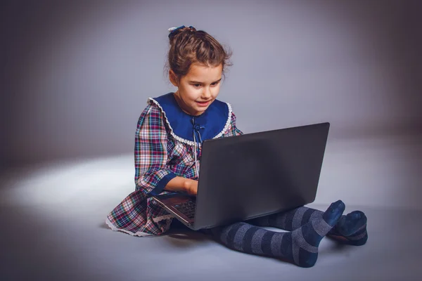 Teen girl 5 years of European appearance looks laptop on a gra — Stock Photo, Image