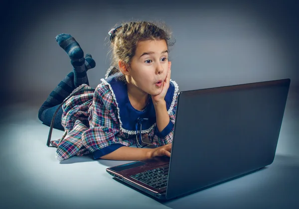 Menina adolescente jogando o chão em um notebook em fundo cinza — Fotografia de Stock