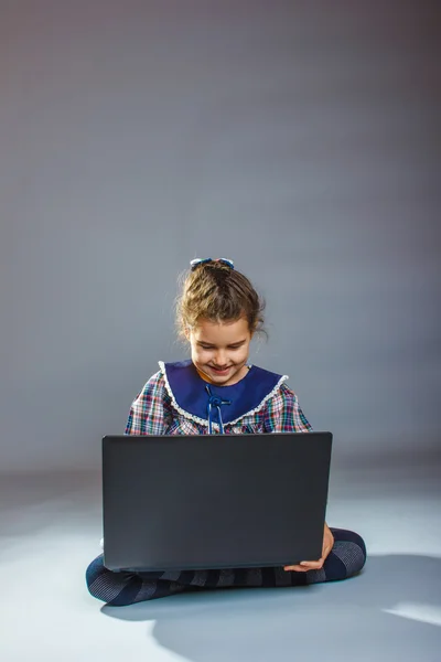 Menina adolescente jogando chão em um notebook cinza backgroun — Fotografia de Stock